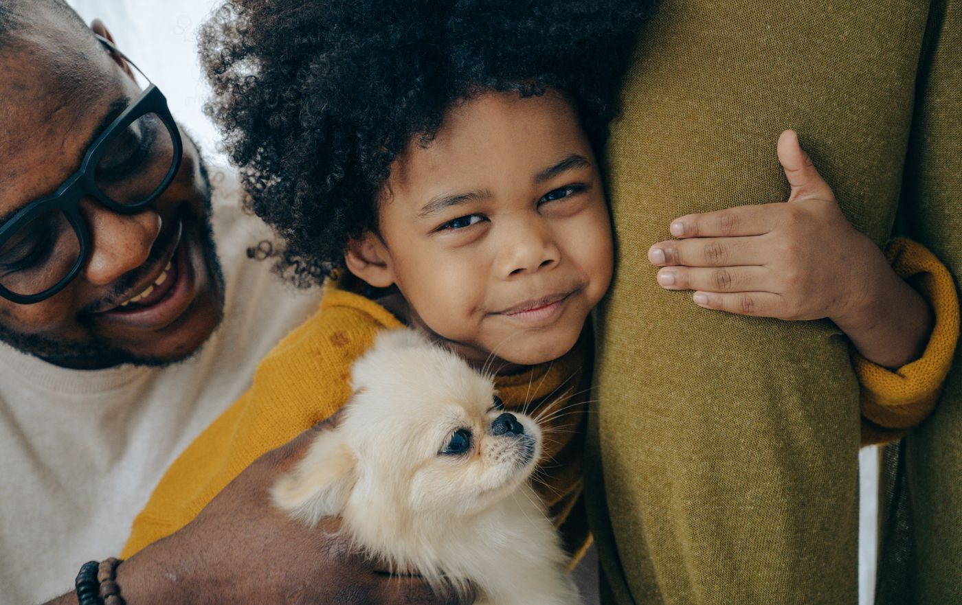 A father and child cuddling their fluffy dog at home.